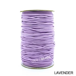 May include: A spool of lavender elastic cord, perfect for crafting jewelry or other projects. The cord is wound tightly on a cardboard spool with a white label that reads "CRAFT BEADS".