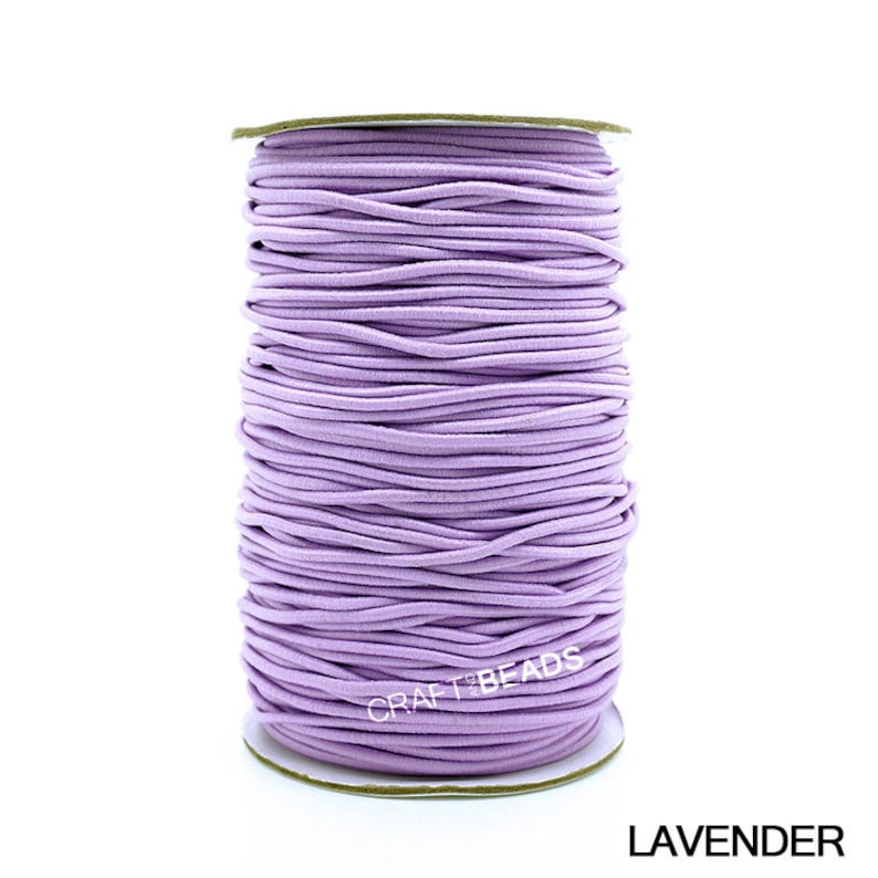 May include: A spool of lavender elastic cord, perfect for crafting jewelry or other projects. The cord is wound tightly on a cardboard spool with a white label that reads "CRAFT BEADS".