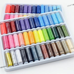 May include: A collection of thread spools in a white plastic tray, displaying a spectrum of colours. The spools are neatly arranged, featuring shades of red, pink, purple, blue, green, yellow, and brown. The text "CRAFT BEADS" is printed on the tray.