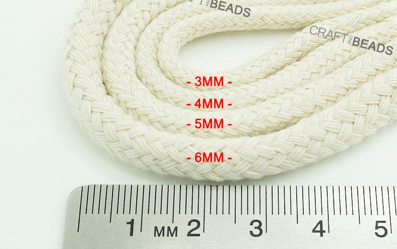 May include: Close-up of white cotton cord in four different sizes, measured in millimeters, with a ruler for reference. The cord is braided and has a textured surface.