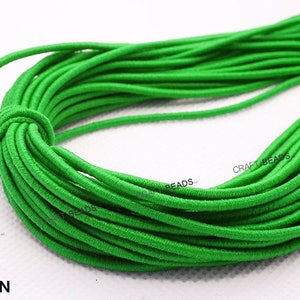 K&ouml;nnte beinhalten: Nahaufnahme einer Spule mit leuchtend gr&uuml;nem Gummiband. Das Band ist fest gewickelt und scheint aus einem weichen, dehnbaren Material zu bestehen. Der Text "CRAFT BEADS" ist auf der Spule sichtbar.