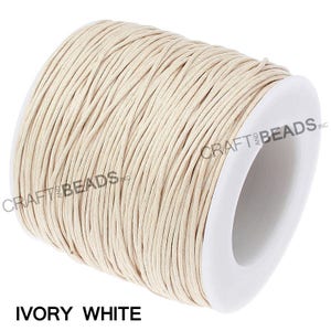 May include: A spool of ivory white waxed cotton cord. The cord is wound around a white plastic spool with the text "CRAFT AND BEADS INC" printed on the side.