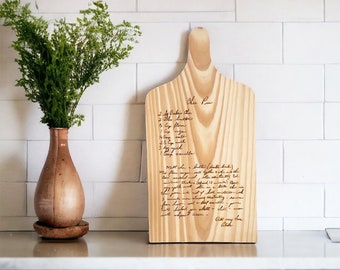 May include: A wooden cutting board with a handwritten recipe for "Chu Pu" inscribed on it. The recipe includes ingredients like butter, flour, eggs, milk, and vanilla. The board has a handle and is a light brown color.
