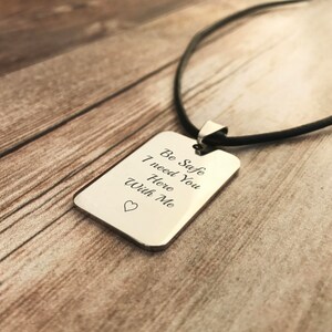 Pu&ograve; includere: Una collana con un ciondolo rettangolare in argento su un cordoncino in pelle nera. Il ciondolo ha le parole "Be Safe I need You Here With Me" incise con un piccolo simbolo di cuore.