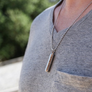 May include: A silver chain necklace with a silver cylindrical pendant engraved with "Teresa & Michael" and two hearts.