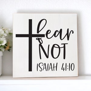 Peut inclure: Une pancarte en bois blanc avec une croix noire et le texte "Fear Not" avec la référence biblique "Isaiah 41:10" en dessous.