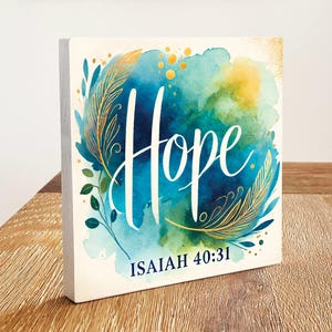 May include: A square wooden sign with a watercolour background in shades of blue and green. The word "Hope" is written in white script with gold accents. The verse "ISAIAH 40:31" is written in black at the bottom of the sign.
