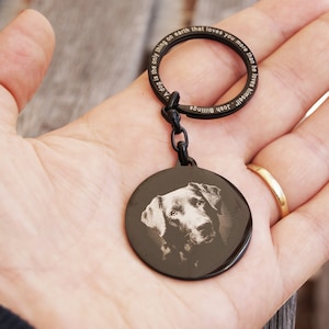 Pode incluir: Porta-chaves de metal preto com um pendente circular com um retrato de c&atilde;o. O anel do porta-chaves tem o texto gravado: "Um c&atilde;o &eacute; a &uacute;nica coisa na terra que te ama mais do que a si mesmo". Uma corrente liga o anel ao pendente.