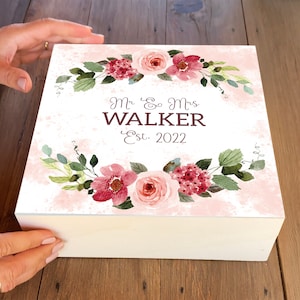 May include: White wooden box with a pink and white floral design. The box has the text "Mr. & Mrs. WALKER Est. 2022" on the front.