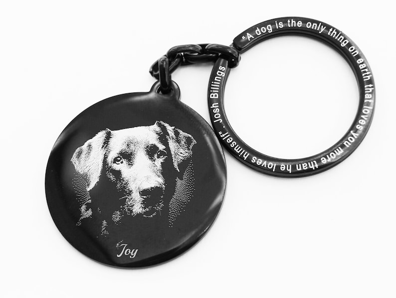 Pode incluir: Chaveiro preto com um pingente circular com um retrato de cachorro e o nome "Joy". O anel do chaveiro tem a cita&ccedil;&atilde;o "Um c&atilde;o &eacute; a &uacute;nica coisa na terra que te ama mais do que ele se ama" de Josh Billings.