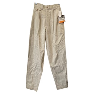 May include: Tan-colored pleated pants with a button closure and two front pockets. The pants have a straight leg design and a tag attached to the front. The pants are hanging on a hanger.