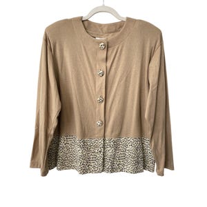 May include: A tan long-sleeved cardigan with a round neckline and four decorative buttons down the front. The bottom of the cardigan features a leopard print pattern. The cardigan is hanging on a white hanger.