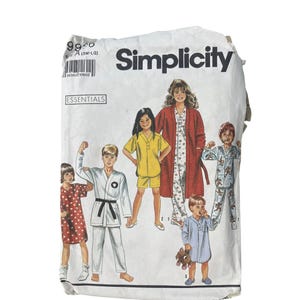 May include: A Simplicity sewing pattern envelope featuring illustrations of children in various outfits, including pajamas, a karate uniform, and a yellow shorts set. The envelope is white with the brand name in large black letters.