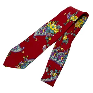 May include: A red necktie with a floral paisley pattern. The tie features a repeating design of colorful flowers in yellow, blue, and purple against a red background. The tie is made of a smooth fabric and is angled across the frame.