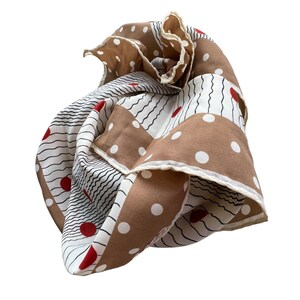 May include: A folded silk scarf with a mix of patterns. The scarf features sections of white with black wavy lines, brown with white polka dots, and white with red dots. The edges are trimmed with a cream-colored border.