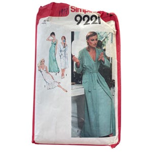 May include: Vintage Simplicity sewing pattern 9221. The pattern envelope features illustrations of women's dresses and a robe. The main image shows a woman in a long, light green robe with a belt. The envelope is red and white.