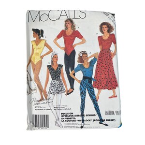 May include: A vintage McCall's sewing pattern featuring illustrations of various 1980s women's outfits. The pattern includes a bodysuit, leggings, a skirt, and a top. The pattern's text includes "Focus on Overlock Sewing" and "Pattern/Pat".