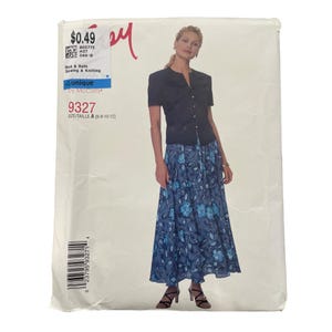 Könnte beinhalten: Eine Schnittmusterhülle für McCall's 9327, Größe A 6-8-10-12. Das Cover zeigt ein schwarzes, kurzärmeliges Oberteil mit Knöpfen und einen langen, fließenden blauen Rock mit weißem und hellblauem Blumenmuster. Der Text enthält 9327 und Bed & Bath.
