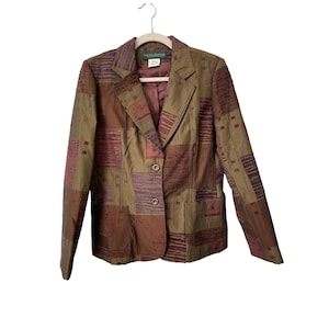 May include: A patchwork blazer in shades of brown, olive green, and burgundy, with a two-button closure and two front pockets. The blazer is hanging on a white hanger. The label reads "Sante Italia".