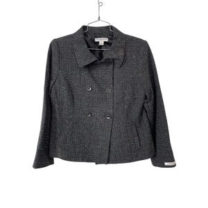 Pode incluir: Um blazer cinza escuro de abotoamento duplo com tecido texturizado. O blazer tem lapelas entalhadas, duas fileiras de botões e uma pequena etiqueta perto do punho. Está pendurado em um cabide de metal.