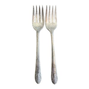 May include: Two antique silver forks with tines and ornate handles. The forks are displayed against a white background. The handles have a decorative, floral-like design at the base. The forks are likely vintage or antique silverware.