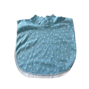 May include: A light blue mock turtleneck shirt with a white floral pattern. The shirt has a rounded hem and a white trim along the bottom edge. The fabric appears to be soft and lightweight.