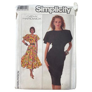 May include: Simplicity sewing pattern featuring designs by Cathy Hardwick. The pattern envelope shows illustrations of two dresses. One is a colorful, patterned dress with a belted waist. The other is a black, form-fitting dress with short sleeves.