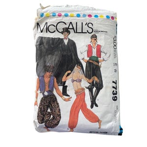 May include: A vintage McCall's sewing pattern packet featuring illustrations of costume designs. The packet showcases various outfits, including a pirate, a genie, and a vampire. The text "McCall's" is prominently displayed, along with the pattern number 7739.