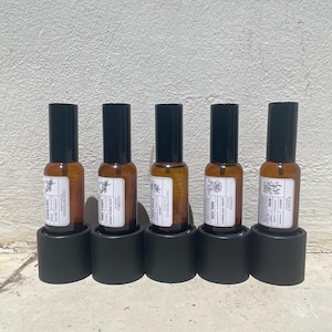 May include: Five amber glass spray bottles with black caps, each held in a cylindrical black base. The bottles feature white rectangular labels with black text and botanical illustrations, displaying the names Verivento, Ombra, Nightborne, Anima, and Radici.