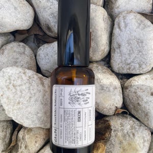 May include: A 30 ml amber glass spray bottle with a black cap and a white rectangular label. The label features botanical illustrations, the text "INCENSO," "CEDRO DEL LIBANO," "PATCHOULI, AMBRA," "BASILICO," "ZENZERO," and "FATTO IN ITALIA."