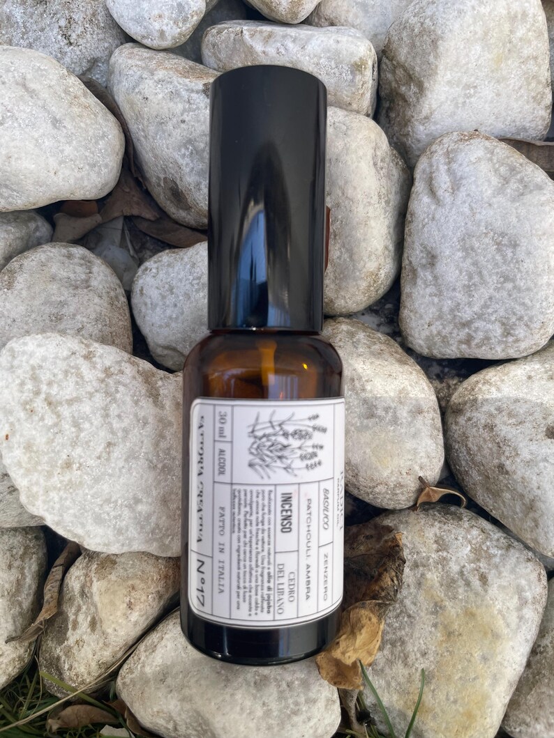 May include: A 30 ml amber glass spray bottle with a black cap and a white rectangular label. The label features botanical illustrations, the text "INCENSO," "CEDRO DEL LIBANO," "PATCHOULI, AMBRA," "BASILICO," "ZENZERO," and "FATTO IN ITALIA."