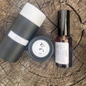 May include: A black cylindrical container with a white label reading RADICI, a small black circular lid with a white logo, and an amber glass spray bottle with a black cap and a white label featuring the text RADICI and various ingredients.