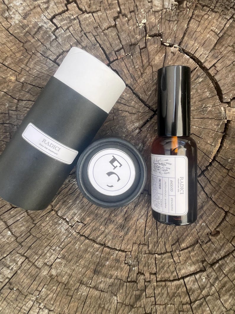 May include: A black cylindrical container with a white label reading RADICI, a small black circular lid with a white logo, and an amber glass spray bottle with a black cap and a white label featuring the text RADICI and various ingredients.