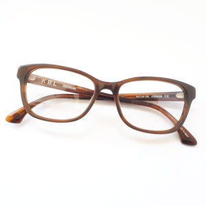 Könnte beinhalten: Braune Schildpatt-Brille mit klaren Gläsern. Der Rahmen trägt den Text "KBL DAYDREAM" auf der rechten Seite und "50□16-140 JC-KN2038 CE" auf der linken Seite.
