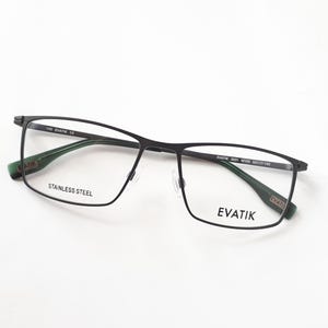 Könnte beinhalten: Schwarze rechteckige Brille mit grünen Akzenten an den Bügeln. Der Rahmen besteht aus Edelstahl. Der Markenname "EVATIK" ist auf dem Bügel und dem Glas sichtbar.