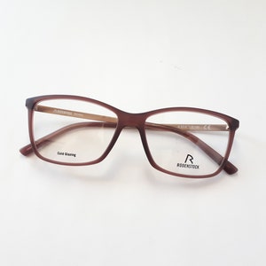 Könnte beinhalten: Braune rechteckige Brille mit klaren Gläsern. Der Markenname "RODENSTOCK" ist auf dem rechten Bügel aufgedruckt.