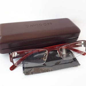 May include: Red and silver eyeglasses with clear lenses in a brown case. The case has the word "DAVIDOFF" printed on the top.