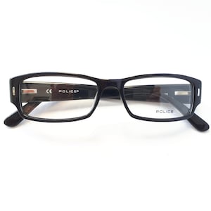 Puede incluir: Gafas rectangulares negras con lentes transparentes. Las monturas tienen un acabado brillante y la marca "POLICE" es visible en la lente derecha. Las gafas tienen un diseño moderno y minimalista.