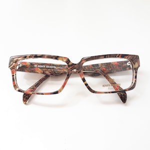 May include: A pair of brown and red patterned eyeglasses with clear lenses. The brand name "Renato Balestra Roma" is printed on the frame.
