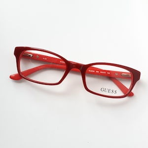 Könnte beinhalten: Rote GUESS-Brille mit rechteckigem Rahmen. Die Brille hat eine glänzende Oberfläche und der Markenname ist auf dem rechten Glas aufgedruckt. Rahmenmaße: 53-16-135.