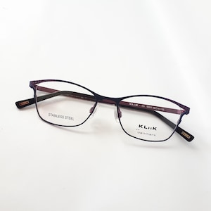 Könnte beinhalten: Lilafarbene Metallgestellbrille mit klaren Gläsern. Der Rahmen trägt den Text "KLIIK -  denmark" auf der rechten Linse.