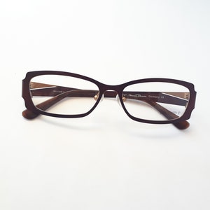 Könnte beinhalten: Braune rechteckige Brille mit einem goldenen Metallrahmen. Der Rahmen trägt den Text "Design Marco Roma Germany CE" auf der rechten Seite.