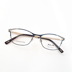 Könnte beinhalten: Schwarze Metallgestellbrille mit goldener Einfassung und klaren Gläsern. Der Rahmen trägt den Schriftzug "STAINLESS STEEL" auf der linken Seite und "KLIK...denmark" auf der rechten Seite.