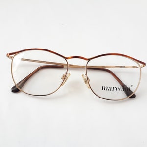 Könnte beinhalten: Goldfarbene Brille mit braunen Schildpattbügeln. Der Markenname "marcolin" ist auf der rechten Linse aufgedruckt.
