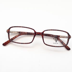 Könnte beinhalten: Schildpatt-Brille mit klaren Gläsern und dem Markennamen "VALDI" auf dem rechten Glas.