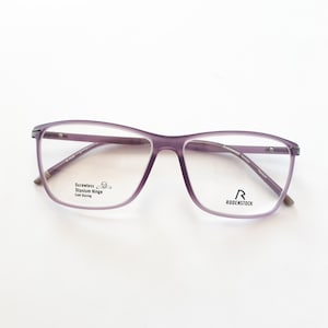 Könnte beinhalten: Lilafarbene Brille mit klaren Gläsern und einem schwarzen Rodenstock-Logo am rechten Bügel. Die Brille verfügt über ein schraubenloses Titan-Scharnier und ein Kordel-Schiebesystem.