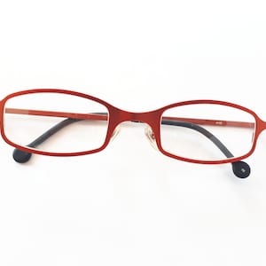 May include: Red metal frame eyeglasses with black arms and clear lenses.