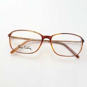 Könnte beinhalten: Braune Schildpatt-Brille mit goldfarbenem Metallrahmen und klaren Gläsern. Der Markenname "Pierre Cardin" ist auf dem linken Glas aufgedruckt.