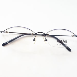 Könnte beinhalten: Schwarze randlose Brille mit einem lila und schwarzen Musterrahmen. Die Brille hat das Wort "visée" und "Lunettes" auf der rechten Linse.