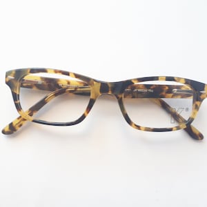 May include: Tortoiseshell eyeglasses with clear lenses and a K logo on the right lens.